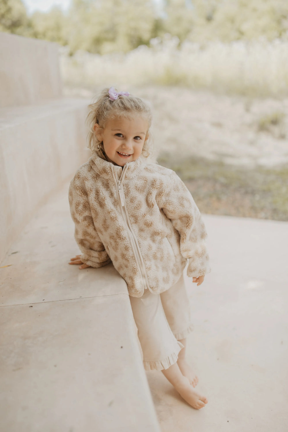 Leevje mini-me Leopard print teddy jacket for kids leo getragen von einem kleinen Mädchen auf einer sommerlichen Terrasse, Ansicht von vorne