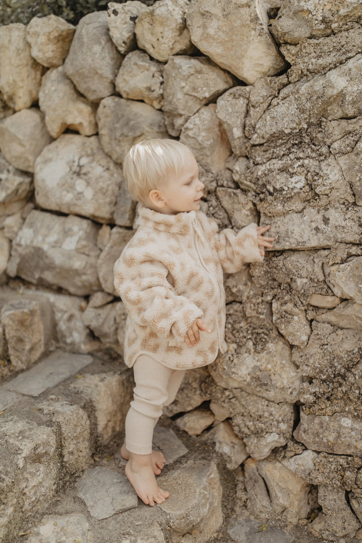 Leevje mini-me Leopard print teddy jacket for kids leo getragen von einem kleinen Jungen vor einer Steinmauer stehend, Ansicht von der Seite 