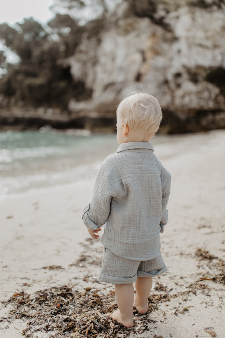 Leevje muslin shorts soft green getragen von einem kleinen Jungen am Strand, Ansicht von hinten 