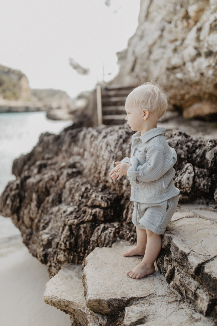 Leevje muslin shorts soft green getragen von einem kleinen Jungen am Strand, Ansicht von der Seite 
