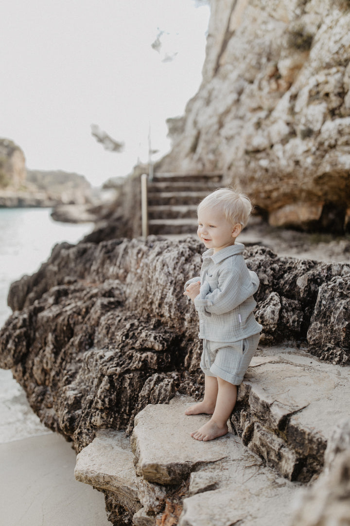 Leevje muslin shorts soft green getragen von einem kleinen Jungen am Strand, Ansicht von der Seite 