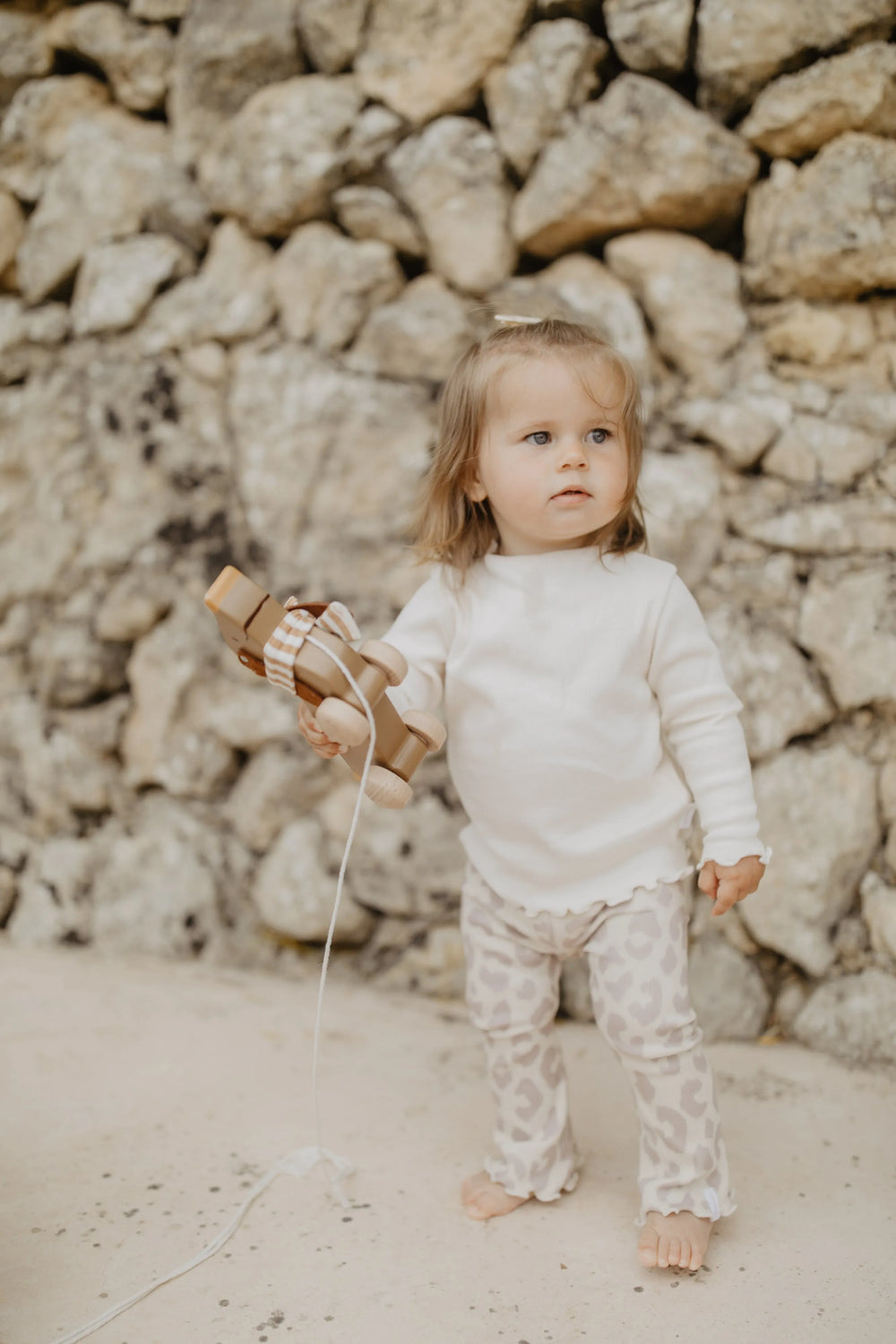 Leevje rib knit flared leggings leo getragen von einem Baby-Mädchen vor einer Steinmauer stehend, Ansicht von vorne