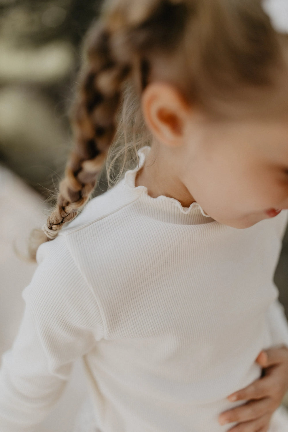 Leevje rib knit long sleeve light beige getragen von einem Mädchen, Blick von oben, Fokus auf gerippter Struktur und gerüschtem Halsausschnitt 