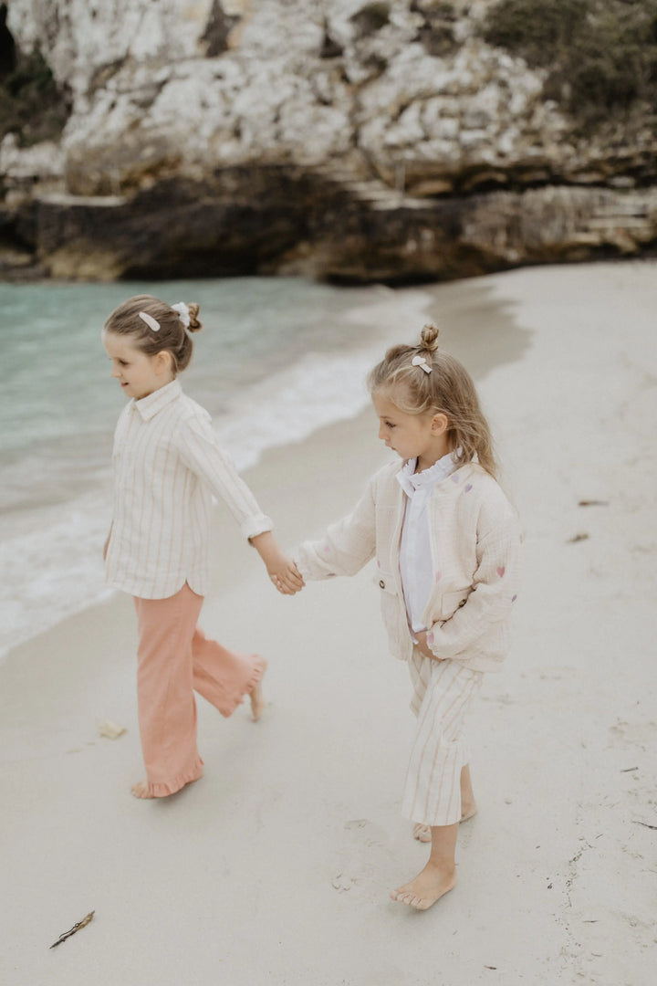 Leevje wide frill hem trousers in Linen Optic terracotta getragen von einem Mädchen am Strand, Ansicht von vorne