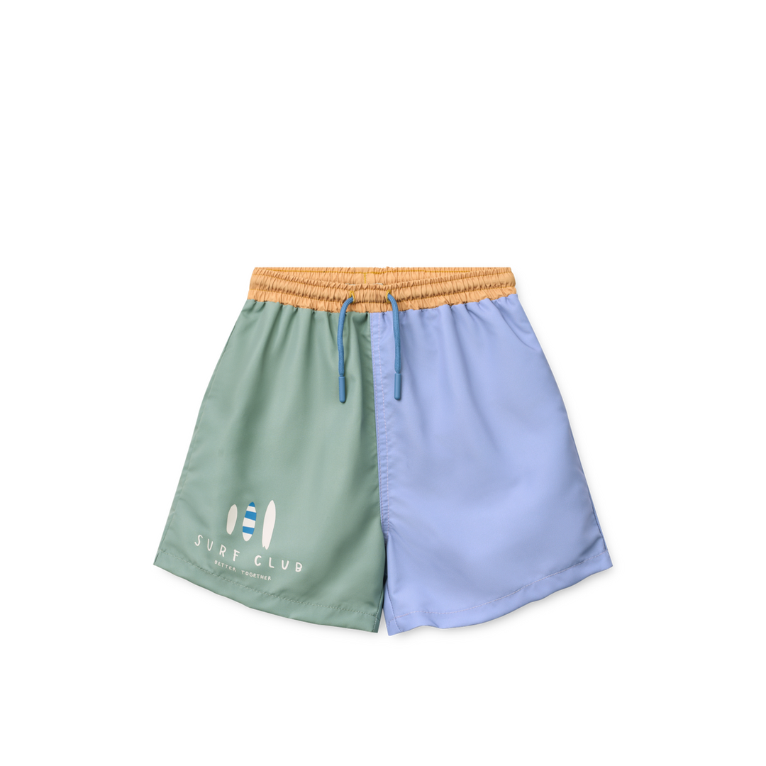 Badehose für Jungen mit weitem Bein, linkes Bein in hellblau, rechtes ein in grün mit drei aufgedruckten sirfbrettern am unteren Rand und der Aufschrift "surf Club". hellbrauner Gummibund mit verstellbarer Kordel. 