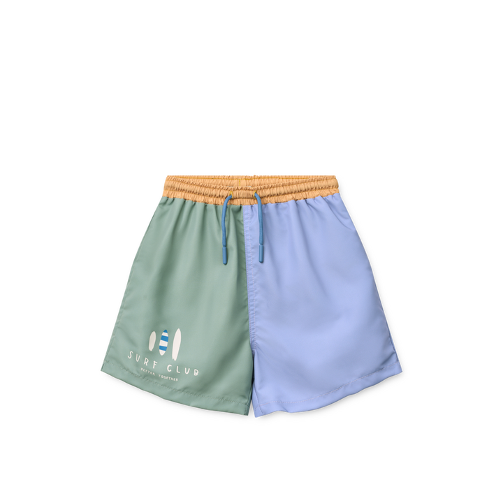 Badehose für Jungen mit weitem Bein, linkes Bein in hellblau, rechtes ein in grün mit drei aufgedruckten sirfbrettern am unteren Rand und der Aufschrift "surf Club". hellbrauner Gummibund mit verstellbarer Kordel. 