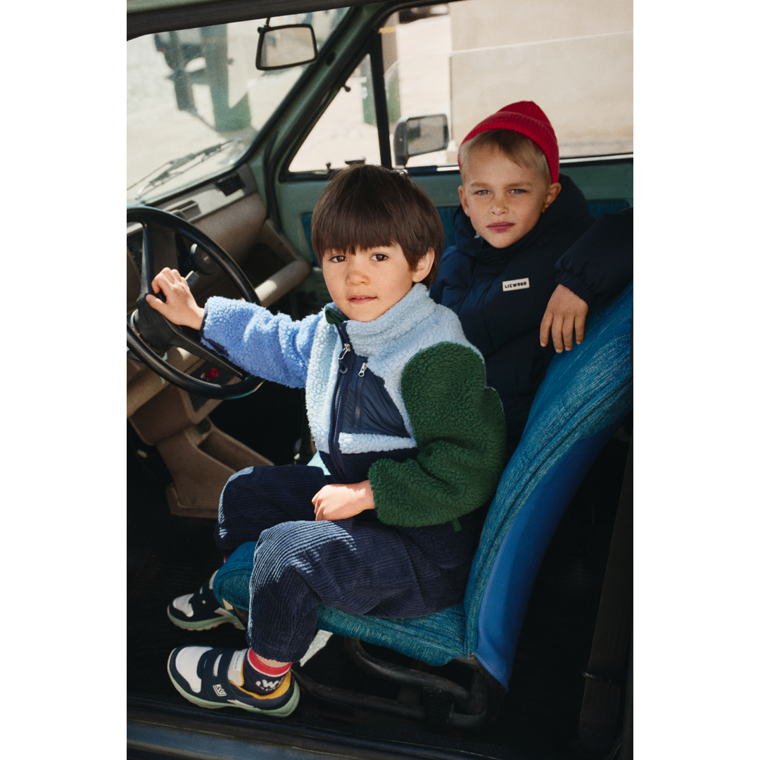 Liewood Nolan Pile Jacket classic navy multi mix etragen von einem kleinen Jungen in einem Auto am Lenkrad sitzend, Ansicht von der Seite. 