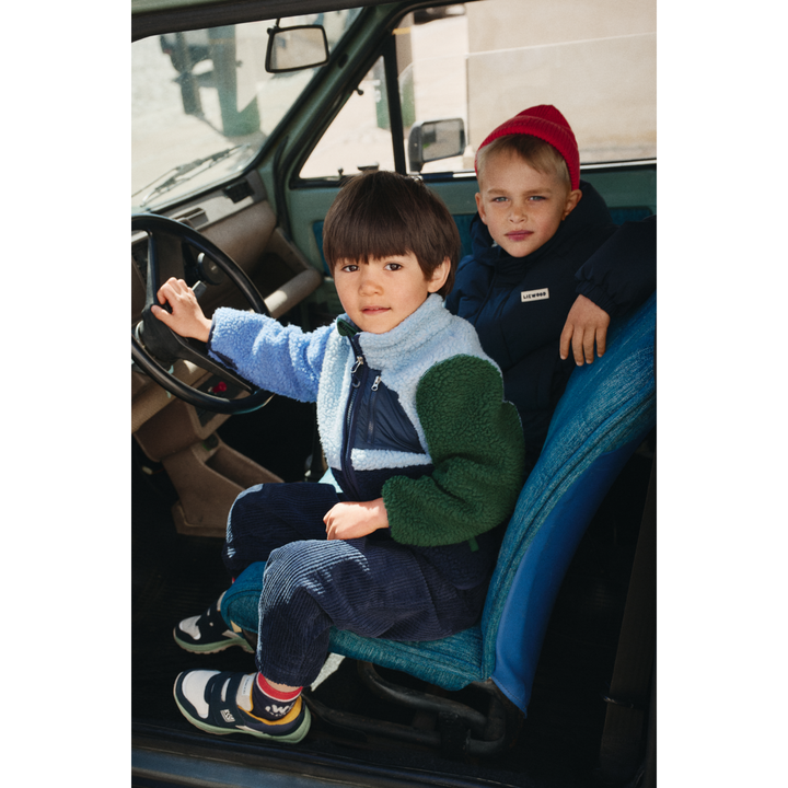 Liewood Nolan Pile Jacket classic navy multi mix etragen von einem kleinen Jungen in einem Auto am Lenkrad sitzend, Ansicht von der Seite. 