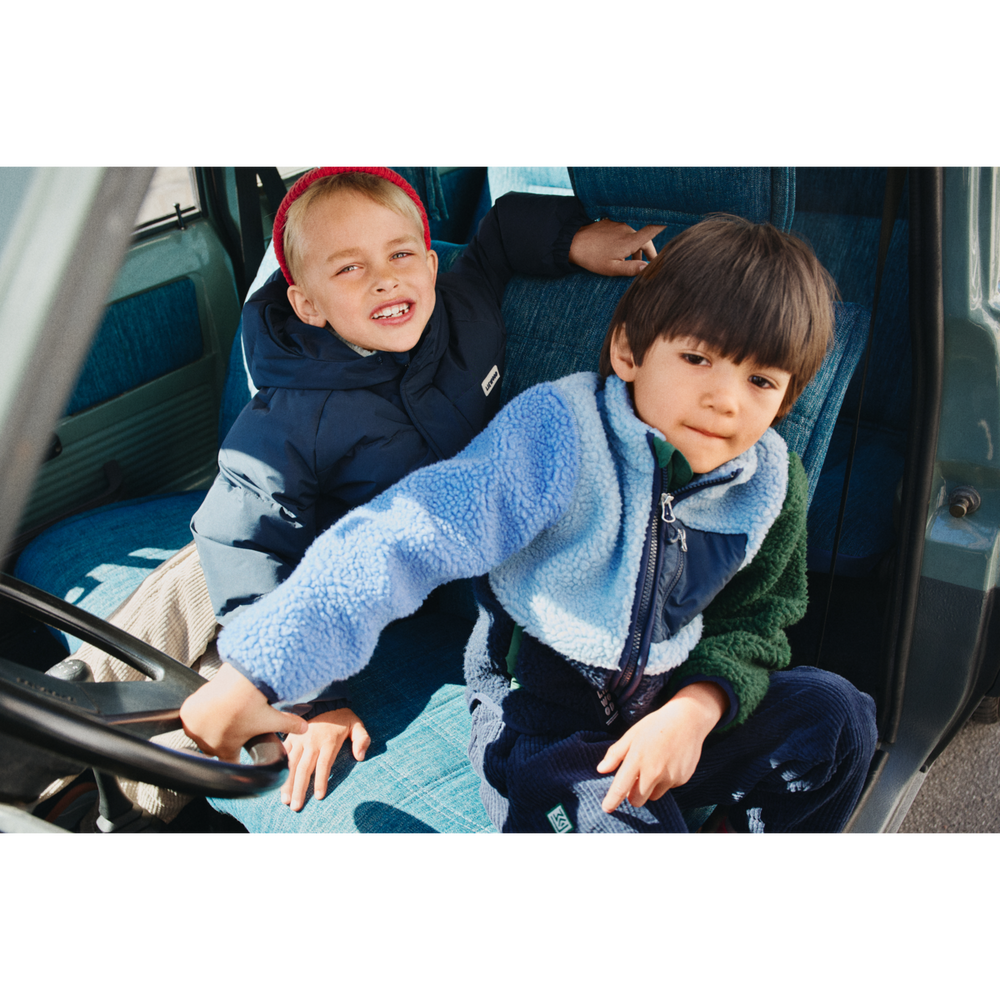 Liewood Nolan Pile Jacket classic navy multi mix getragen von einem kleinen Jungen in einem Auto am Lenkrad sitzend, Ansicht von vorne. 