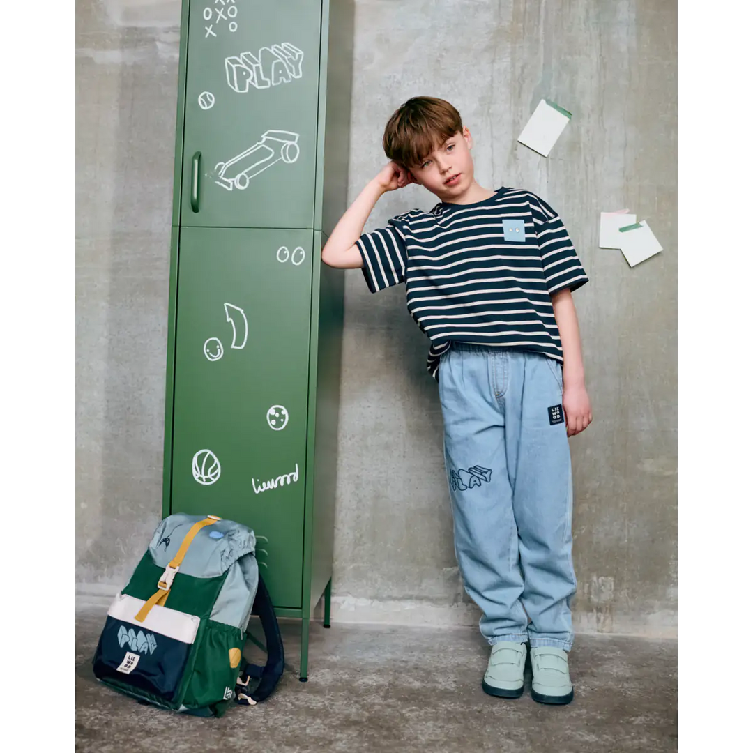 Liewood Tyler Stripe SS T-shirt Y/D stripe classic navy sandy getragen von einem Jungen, der sich an einen Spind anlehnt. Ansicht von vorne. 