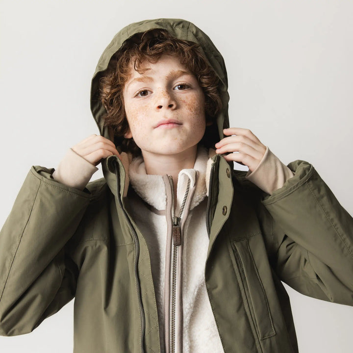 Mini A Ture Matkastorio fleece lined winter jacket GRS kalamata green getragen von einem Jungen mit aufgesetzter Kapuze und geöffnetem Reißverschluss, Ansicht von vorne. 