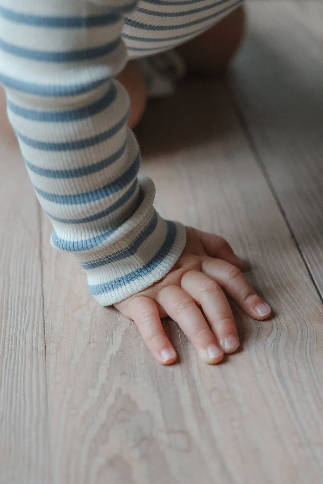 Petit Piao PPSky LS Body Infinity Striped getragen von einem Baby, Detailansicht Arm und Hand mit Blick auf die gerippte Jersey-Qualität und das Streifenmuster