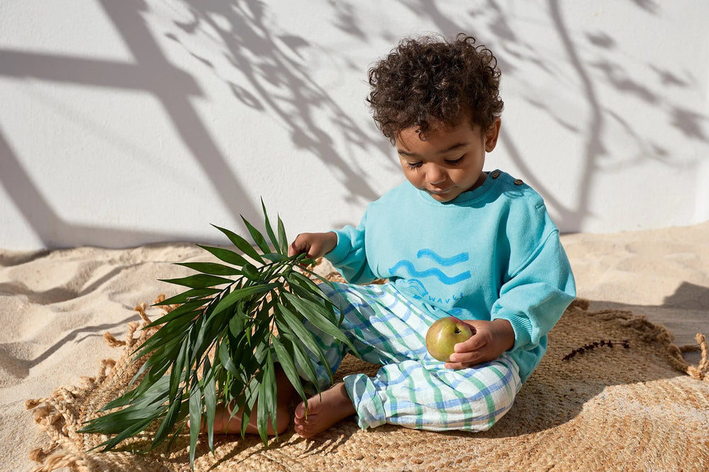 Ply Up Printed Woven Trousers studio getragen von einem kleinen Jungen, der auf Sandboden sitzt