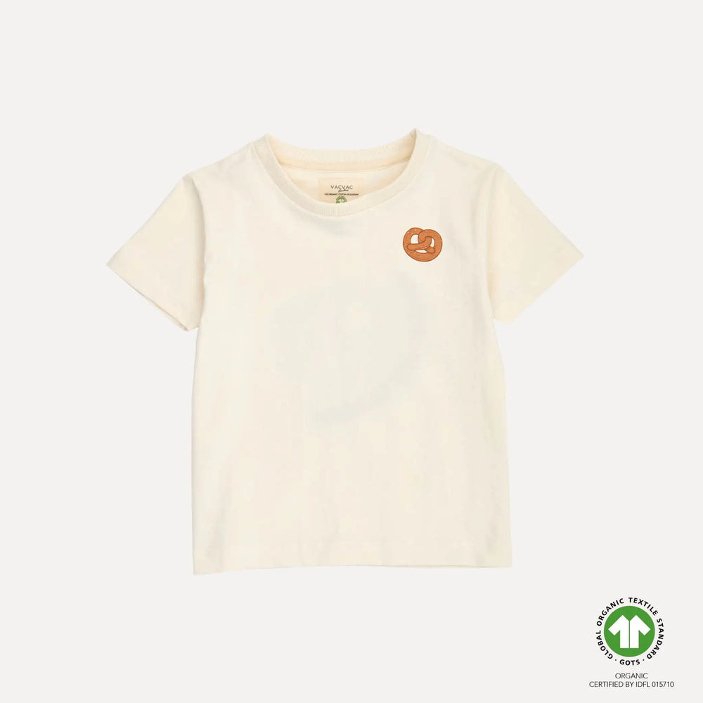 cremefarbenes, kurzärmeliges T-Shirt für Kinder aus Bio-Baumwolle mit Rundhalsausschnitt und kleinem Bretzel-Print auf Höhe der linken Brust. Produktbild, Ansicht von vorne. 