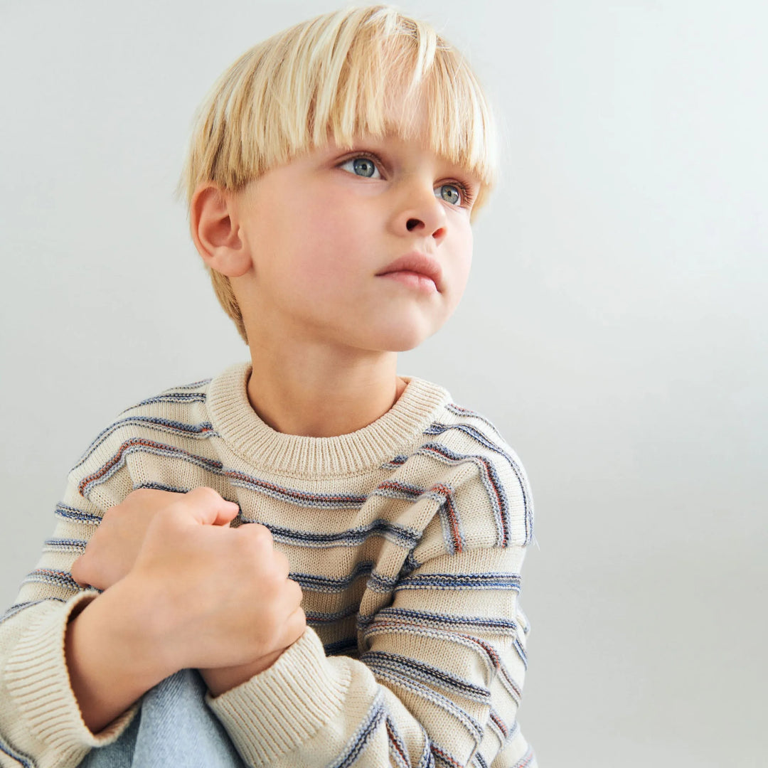 Wheat Jacquard Pullover Harlow sandshell stripe getragen von einem Jungen in sitzender Position vor weißem Hintergrund, Ansicht von vorne