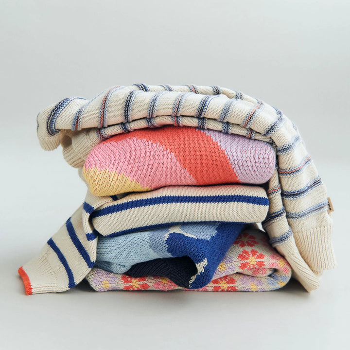 Wheat Jacquard Pullover Harlow sandshell stripe auf einem nicht geordneten Stapel liegend, welcher weitere gestrickte Oberteile enthält