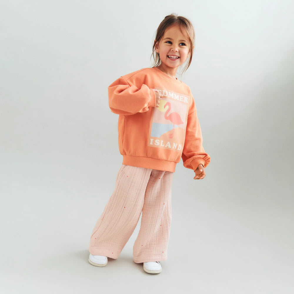 Wheat Sweatshirt Eliza sunkissed orange getragen von einem Mädchen vor weißem Hintergrund, Ansicht von vorne mit Blick auf den bunten Aufdruck
