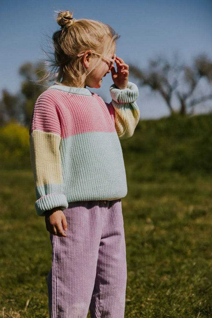 Yuki Color Block Sweater STICKY CANDY getragen von einem Mädchen stehend auf einer grünen Wiese Ansicht von der Seite vorne mit Fokus auf den Pullover