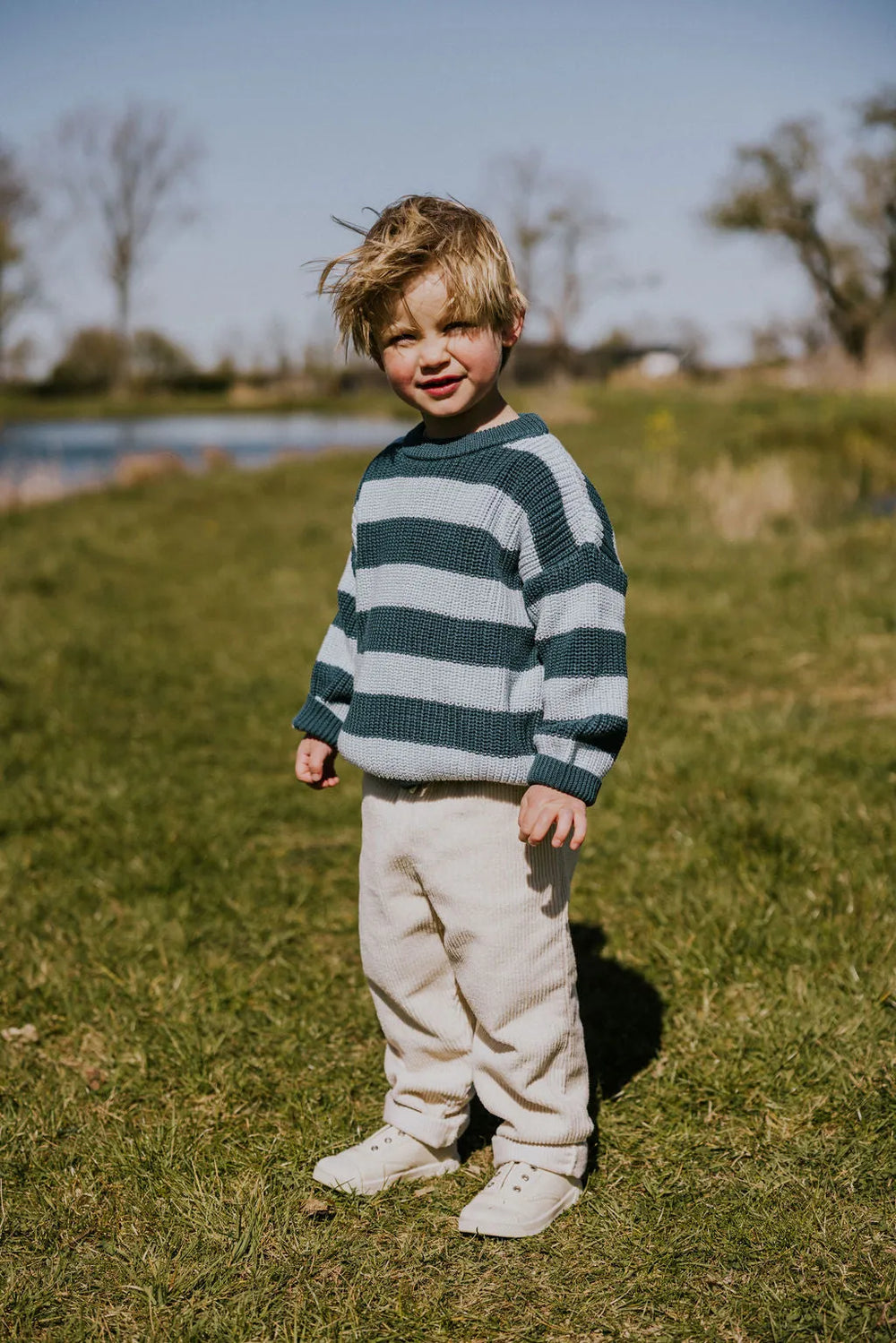 Yuki Stripes Sweater BLUE BIRD getragen von einem männlichen Kleinkind Ansicht frontal seitlich auf einer grünen Wiese
