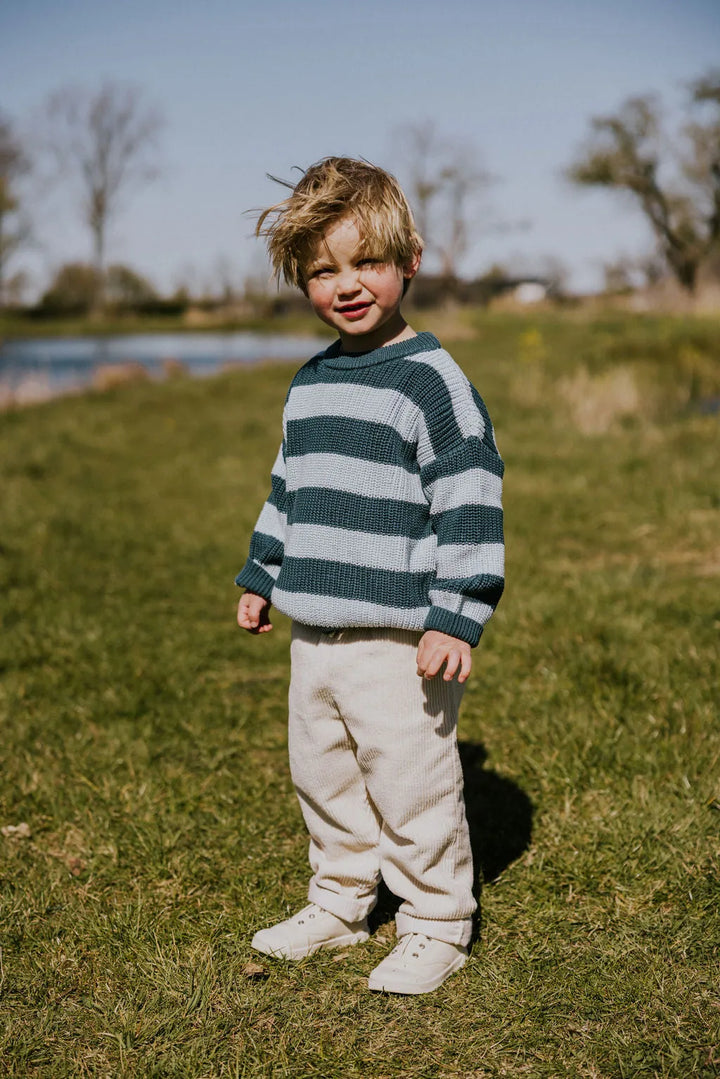 Yuki Stripes Sweater BLUE BIRD getragen von einem männlichen Kleinkind Ansicht frontal seitlich auf einer grünen Wiese