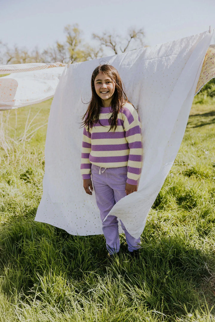 Yuki Stripes Sweater ICE CREAM getragen von einem Mädchen auf einer Grünen Wiese stehend mit einem weißen Laken, das auf einer Wäscheleine hängt, im Rücken Ansicht von vorne